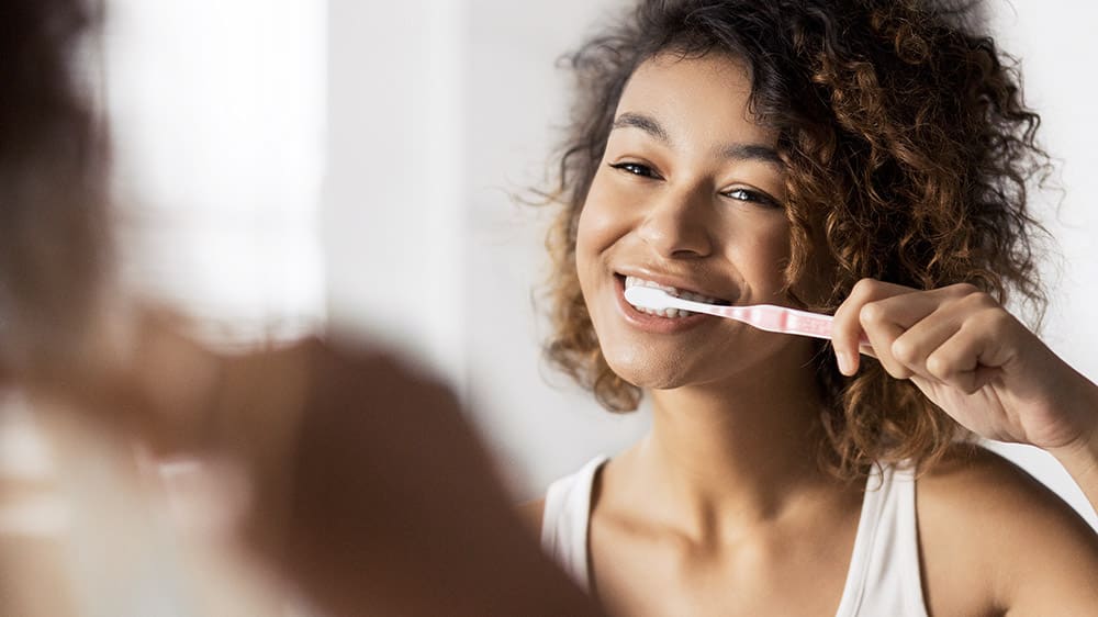 Nő mossa a fogát fogkefével a tükör előtt